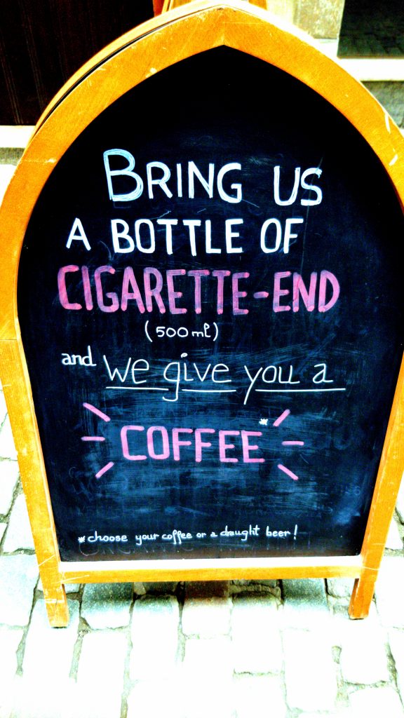 Schild vor dem The Sisters Brussels Café: bringt uns 500 ml Zigarettenkippen und wir geben Euch einen Kaffee aus